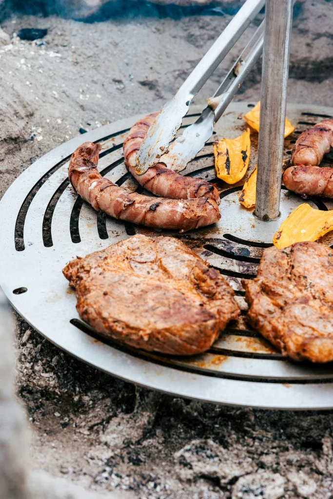 Steaks und Würstchen auf der Grillplatte am Lagerfeuer