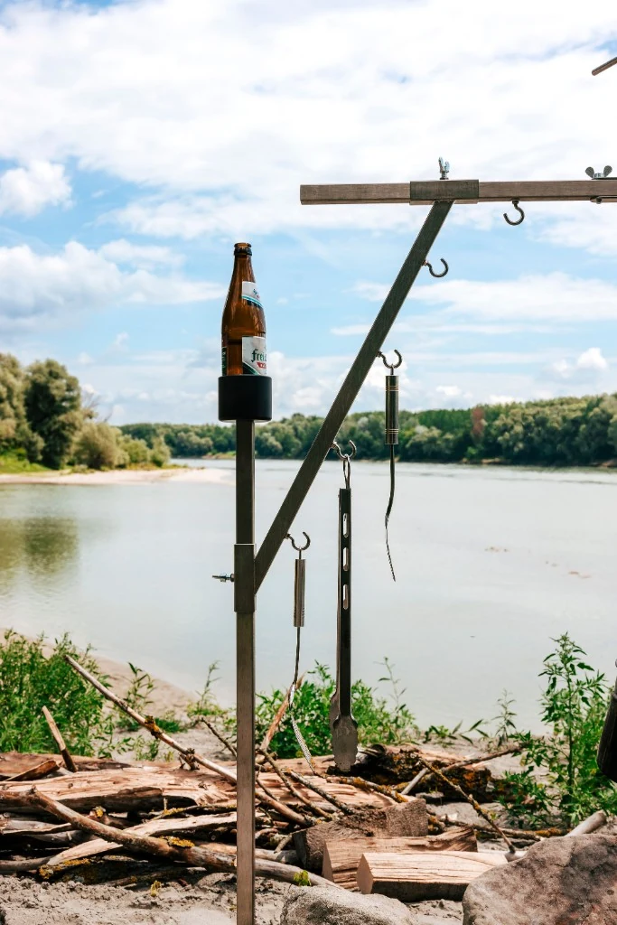 Getränkehalter am Dreibein mit Kochwerkzeugen am Flussufer
