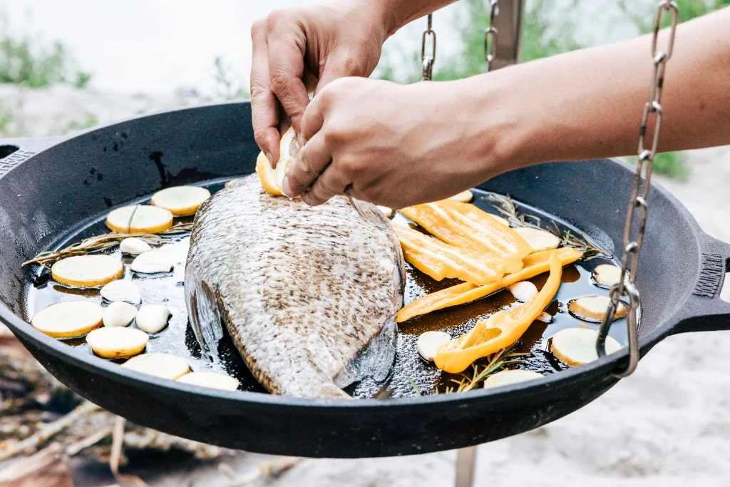 Fisch mit Zitrone, Kartoffeln und Kräutern in der Gusspfanne über dem Feuer